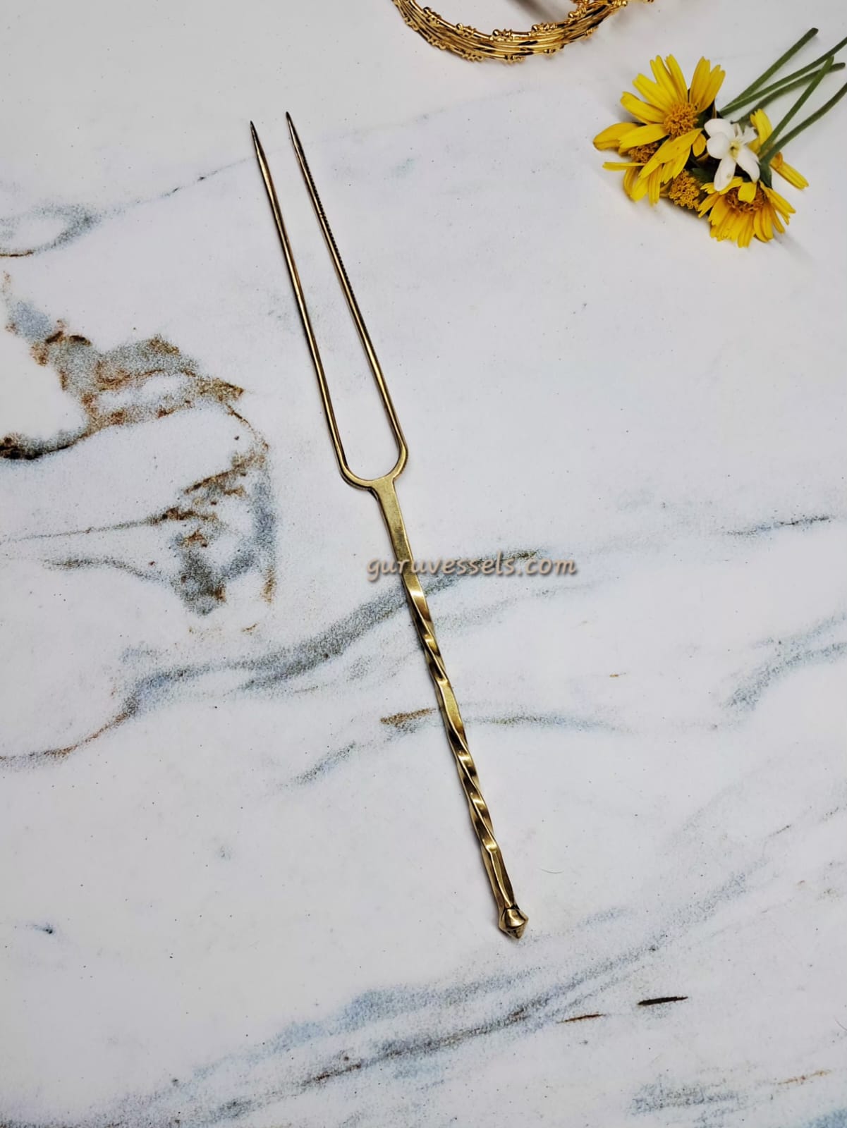 brass detangler on a marble surface with yellow flowers